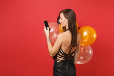Arka arka görünüm içinde holding, istimal hareket eden telefon ile boş siyah boş perde, hava balonları izole kırmızı zemin üzerine siyah genç kadın. Mutlu yeni yıl, Doğum günü mockup tatil parti konsept