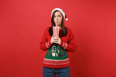 Noel şapka bir kenara kola veya kola plastik bardak kırmızı zemin üzerine izole içme arıyor genç Noel Baba kız şaşkın. Mutlu yeni yıl 2019 kutlama tatil parti kavramı. Kopyalama alanı alay