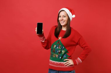 Parlak kırmızı zemin üzerine izole boş boş ekran ile cep telefonu tutan Noel şapkalı güzel genç Noel Baba kız. Mutlu yeni yıl 2019 kutlama tatil parti kavramı. Kopyalama alanı alay