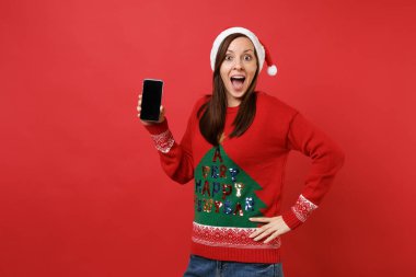 Ağız geniş açık tutarak genç Noel Baba kız kırmızı zemin üzerine izole boş boş ekran ile cep telefonu tutan şaşırttı. Mutlu yeni yıl 2019 kutlama tatil parti kavramı. Kopyalama alanı alay