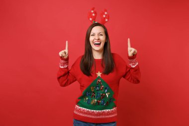 Parlak kırmızı zemin üzerine dekoratif geyik boynuzları işaret parmakları işaret eden oktan yukarı kafasına izole eğlenceli genç Noel Baba kız gülüyor. Mutlu yeni yıl 2019 kutlama tatil parti kavramı. Kopyalama alanı alay
