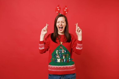 Heyecanlı genç Noel Baba kız parmak tutmak dilek yapma dekoratif geyik boynuzları geçti eğlenceli kırmızı zemin üzerine izole kapalı ağız geniş açık gözleri. Mutlu yeni yıl 2019 kutlama tatil parti konsept