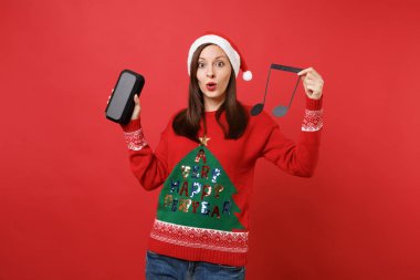 Hayret genç Noel Baba kız holding nota, taşınabilir kablosuz bluetooth müzik hoparlör parlak kırmızı zemin üzerine izole. Mutlu yeni yıl 2019 kutlama tatil parti kavramı. Kopyalama alanı alay