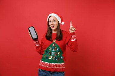 Genç Noel Baba kız işaret parmağı ile harika bir yeni fikir, kırmızı zemin üzerine izole tutun taşınabilir kablosuz bluetooth müzik hoparlör heyecan. Mutlu yeni yıl 2019 kutlama tatil parti konsept