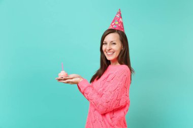 Gülümseyen genç kadın örgü pembe kazak Doğum günü şapkalı yan görünümü tutun el kek mavi turkuaz renkli stüdyo portre üzerinde izole mum ile. İnsanlar yaşam tarzı kavramı. Kopyalama alanı alay