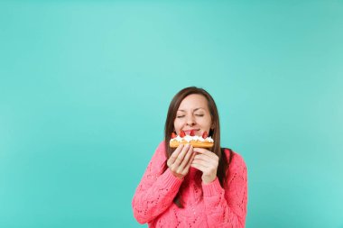 Genç ve güzel kadın gözleri kapalı tutmak örme pembe kazaklı sniff pasta kek mavi turkuaz duvar arka planda, stüdyo portre izole elinde tut. İnsanlar yaşam tarzı kavramı. Kopyalama alanı alay