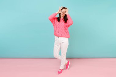 Tam uzunlukta örme gül kazaklı gülümseyen genç kadın portresi, beyaz parlak pembe mavi pastel duvar arka planda Studio izole poz pantolon. Moda yaşam tarzı kavramı. Kopyalama alanı alay