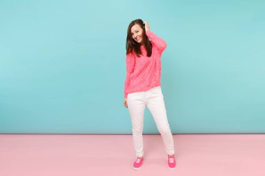 Tam uzunlukta örme gül kazaklı gülümseyen genç kadın portresi, beyaz parlak pembe mavi pastel duvar arka planda Studio izole poz pantolon. Moda yaşam tarzı kavramı. Kopyalama alanı alay