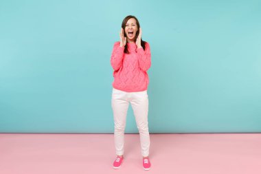 Tam uzunlukta örme gül kazaklı gülümseyen genç kadın portresi, beyaz parlak pembe mavi pastel duvar arka planda Studio izole poz pantolon. Moda yaşam tarzı kavramı. Kopyalama alanı alay