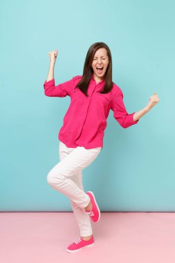 Tam uzunlukta gülümseyen genç güzel kadın portresi gömlek bluz gül, beyaz pantolon poz parlak pembe mavi pastel duvar arka plan studio izole. Moda yaşam tarzı kavramı. Kopyalama alanı alay