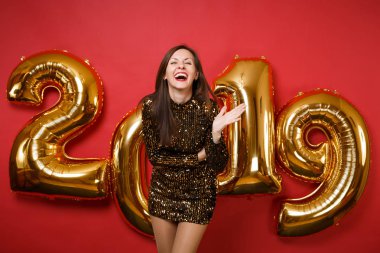 Tatil partisi parlak kırmızı duvar arka planda, golden numaraları hava balonları stüdyo portre izole kutlama parlak parıltı elbiseli neşeli genç harika kız. Mutlu yeni yıl 2019 Noel kavramı.