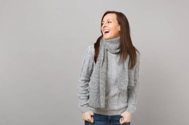 Genç kadın bir kenara gri duvar arka plan stüdyo portre üzerinde izole gri süveterli seyir eşarp gülüyor. Sağlıklı moda yaşam tarzı, insanlar samimi duygular, soğuk sezon kavramı. Kopyalama alanı alay