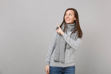 Gülümseyen gri süveterli genç kadın, bakılması, işaret parmağı bir kenara gri duvar arka plan üzerinde izole eşarp. Sağlıklı moda yaşam tarzı insanların duyguları, soğuk sezon kavramı. Kopyalama alanı alay
