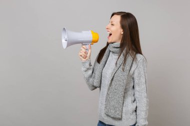 Görünümü gri süveterli neşeli genç kadının yan, arka planda gri duvar izole megafon içinde çığlık eşarp. Sağlıklı moda yaşam tarzı insanların samimi duygular, soğuk sezon kavramı. Kopyalama alanı alay