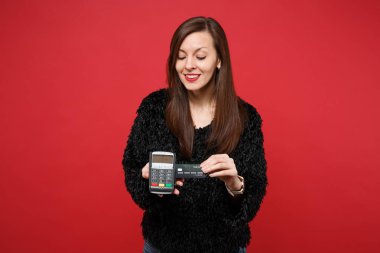 Çekici genç kız siyah kürk kazaklı kablosuz modern banka ödeme terminal işlemek ve kredi kartı ödemeleri kırmızı zemin üzerine izole kazanmak için basılı tutun. İnsanlar samimi duygular yaşam tarzı kavramı