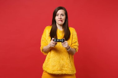 Parlak kırmızı zemin üzerine izole joystick ile bilgisayar oyunu oynamak sarı kürk kazak dudak ısırma endişe genç kadın portresi. İnsanlar samimi duygular, yaşam kavramı. Kopyalama alanı alay