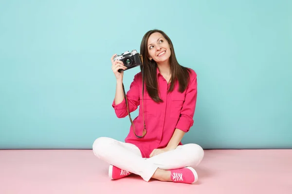 Full length portrait young woman in rose shirt blouse white pants sitting on floor hold camera isolated on pink blue pastel wall background studio. Fashion lifestyle concept. Mock up copy space