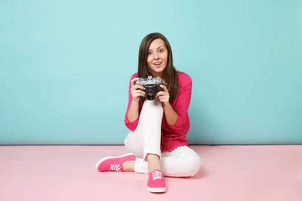 Full length portrait young woman in rose shirt blouse white pants sitting on floor hold camera isolated on pink blue pastel wall background studio. Fashion lifestyle concept. Mock up copy space