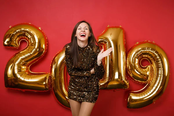Tatil partisi parlak kırmızı duvar arka planda, golden numaraları hava balonları stüdyo portre izole kutlama parlak parıltı elbiseli neşeli genç harika kız. Mutlu yeni yıl 2019 Noel kavramı.