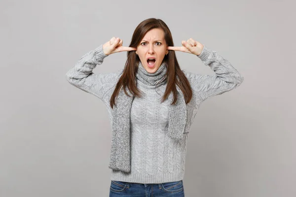 愤怒的女人在灰色毛衣围巾覆盖耳朵与手指保持嘴张开在灰色背景隔离 健康时尚生活方式人们情绪寒冷的季节概念 模拟复制空间 — 图库照片