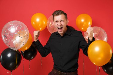 Siyah klasik tişörtlü kutluyor, kazanan jest yapıyor, kırmızı arka plan hava balonu üzerinde çığlık çılgın genç adam. St. Valentine's, kadınlar günü, mutlu yeni yıl, Doğum günü mockup tatil parti konsept