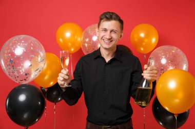 Genç adam şişe, bardak şampanya kırmızı arka plan hava balonu üzerinde tutarak siyah klasik gömlek gülümseyen. Sevgililer, Dünya Kadınlar Günü mutlu yeni yıl Doğum günü mockup tatil parti konsept