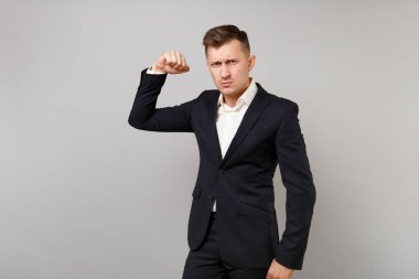 Studio gri arka plan üzerinde izole pazı kas gösterilen ciddi genç iş adamı klasik siyah takım elbise ve gömlek yumruk, kasılıyor. Başarı kariyer servet iş kavramı. Kopyalama alanı alay