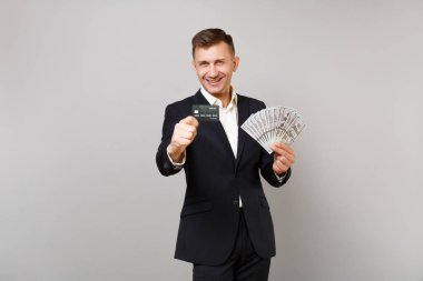 Neşeli genç iş adamı kredi banka kartı çok tutan siyah elbiseli birkaç dolarlık banknotlar nakit para üzerinde gri arka plan izole. Başarı kariyer servet iş kavramı. Kopyalama alanı alay