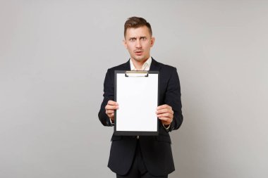 Klasik siyah elbiseli şok çapraşık genç iş adamı ile boş boş sayfası çalışma alanı gri arka plan üzerinde izole Pano tutun. Başarı kariyer servet iş kavramı. Kopyalama alanı alay