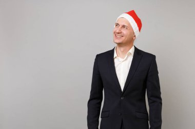 Gülümseyen genç iş adamı klasik siyah takım elbise ve Noel şapka bir kenara gri arka plan üzerinde izole arıyor. Başarı kariyer servet iş. Mutlu yeni yıl 2019 kutlama tatil parti konsept