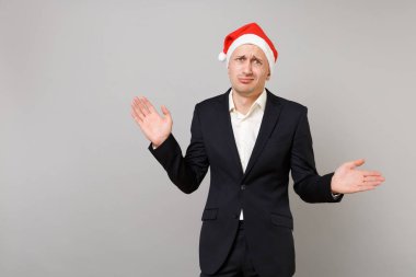 Memnun genç iş adamı Klasik takım, eller yayılan Noel şapka gri arka plan üzerinde izole. Başarı kariyer servet iş. Mutlu yeni yıl 2019 kutlama tatil parti konsept