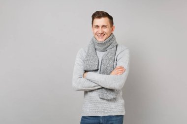 Gri süveterli genç adam gülümsüyor, Studio gri duvar arka plan üzerinde çarpı işareti el ele tutuşarak eşarp izole. Sağlıklı moda yaşam tarzı, insanlar samimi duygular, soğuk sezon kavramı. Kopyalama alanı alay