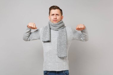 Gri süveterli ciddi genç adam, eşarp gösteren gri duvar arka planda Studio izole yumruklarını sıktı. Sağlıklı moda yaşam tarzı, insanlar samimi duygular, soğuk sezon kavramı. Kopyalama alanı alay