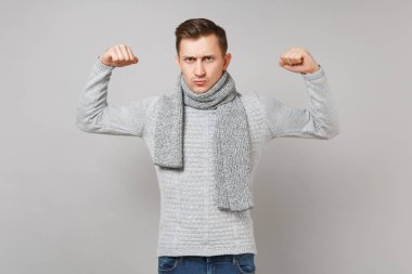 Güçlü genç adam gri süveterli gösteren pazı, gri duvar arka planda Studio izole kas eşarp. Sağlıklı moda yaşam tarzı, insanlar samimi duygular, soğuk sezon kavramı. Kopyalama alanı alay