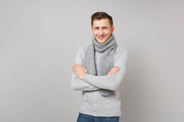 Gri süveterli genç adam gülümsüyor, elele katlanmış eşarp gri arka plan üzerinde stüdyo portre izole. Sağlıklı moda yaşam tarzı, insanlar samimi duygular, soğuk sezon kavramı. Kopyalama alanı alay