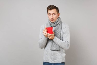 Gri süveterli genç adam üzgün, kırmızı fincan kahve ya da çay Studio gri arka plan üzerinde izole tutan eşarp. Sağlıklı yaşam tarzı, hasta hasta hastalık tedavileri, soğuk sezon kavramı. Kopyalama alanı alay