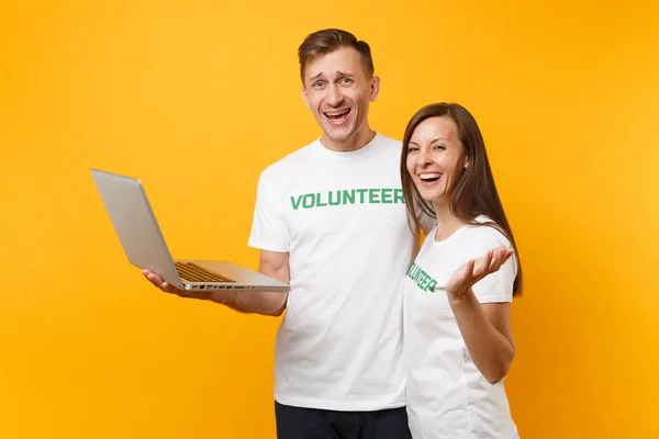 Colleagues couple in white t-shirt with inscription green volunteer using typing laptop pc computer isolated on yellow background. Voluntary free work, assistance help, charity grace teamwork concept