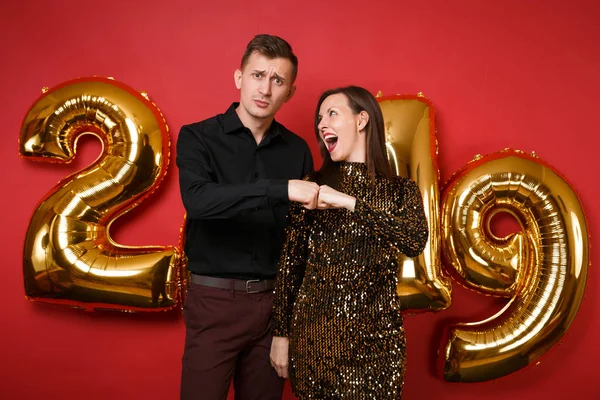 Couple guy girl in shiny glitter dress, black shirt celebrating holiday party isolated on bright red wall background golden numbers air balloons studio portrait. Happy New Year 2019 Christmas concept
