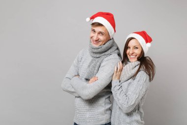Neşeli eğlenceli çift kız adam Santa Noel şapka gri kazak eşarp gri duvar arka planda, stüdyo portre izole kırmızı. Mutlu yeni yıl 2019 kutlama tatil parti kavramı. Kopyalama alanı alay