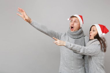 Neşeli eğlenceli çift kız adam Santa Noel şapka gri kazak eşarp gri duvar arka planda, stüdyo portre izole kırmızı. Mutlu yeni yıl 2019 kutlama tatil parti kavramı. Kopyalama alanı alay