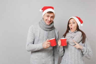 Kırmızı Santa Noel şapka gri kazak eşarp eğlenceli çift kız adam gri duvar arka planda, stüdyo portre izole çay bardak tutun. Mutlu yeni yıl 2019 tatil parti kavramı. Kopyalama alanı alay