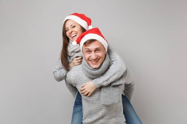 Neşeli eğlenceli çift kız adam Santa Noel şapka gri kazak eşarp gri duvar arka planda, stüdyo portre izole kırmızı. Mutlu yeni yıl 2019 kutlama tatil parti kavramı. Kopyalama alanı alay