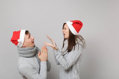 Neşeli eğlenceli çift kız adam Santa Noel şapka gri kazak eşarp gri duvar arka planda, stüdyo portre izole kırmızı. Mutlu yeni yıl 2019 kutlama tatil parti kavramı. Kopyalama alanı alay