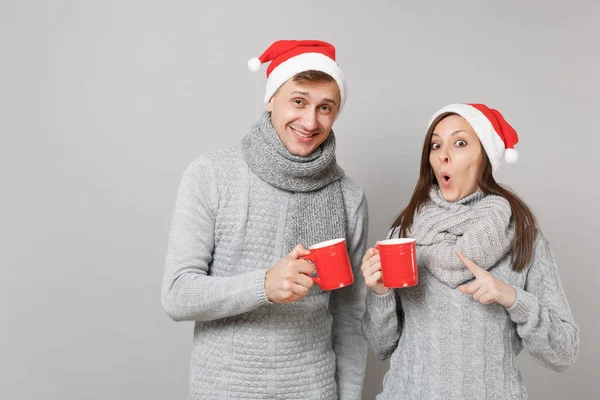 Kırmızı Santa Noel şapka gri kazak eşarp eğlenceli çift kız adam gri duvar arka planda, stüdyo portre izole çay bardak tutun. Mutlu yeni yıl 2019 tatil parti kavramı. Kopyalama alanı alay