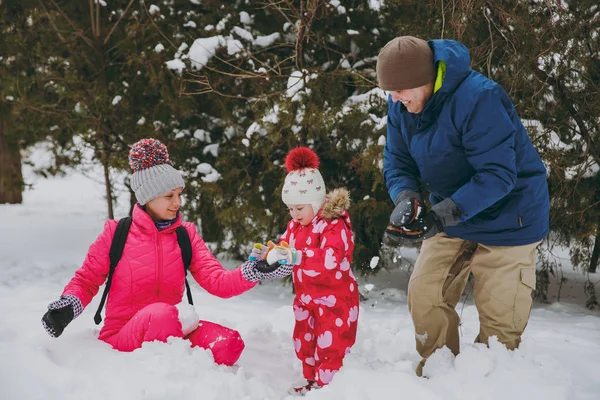 Joyful family woman, man little girl in winter warm clothes play, making snowballs in snowy park or forest outdoors. Winter fun, leisure on holidays. Love relationship family people lifestyle concept