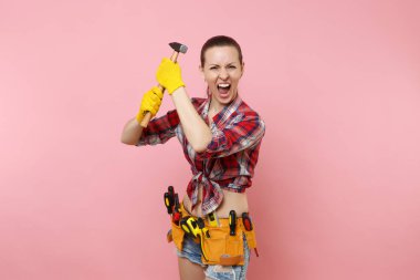 Giyen ekose gömlek, kot şort, kit araçları kemer, pembe arka plan izole farklı enstrümanlar çekiç dolu güçlü genç tamirci kadın. Kadın erkek iş. Yenileme ve işgal kavramı