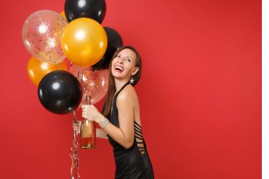 Gülen genç kadın kutluyor, şişe şampanya, kırmızı zemin üzerine izole hava balonları tutan küçük siyah elbise. Sevgililer günü, mutlu yeni yıl, Doğum günü mockup tatil parti konsept