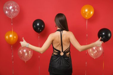 Arka başparmak gösterilmesini, parlak kırmızı arka plan hava balonu üzerinde kutluyor küçük siyah elbise genç kadının arka görünüm. St. Valentine's gün, mutlu yeni yıl, Doğum günü mockup tatil parti konsept