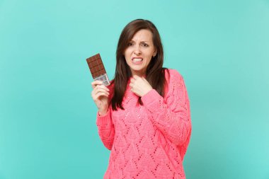 Örgü pembe kazaklı elinde çikolata mavi turkuaz duvar arka planda, stüdyo portre izole tutarak ilgili memnun genç kadın. İnsanlar yaşam tarzı kavramı. Kopyalama alanı alay