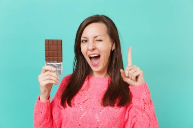 Çekici genç kadın örgü pembe kazaklı işaret parmağı, yanıp sönen mavi arka plan, stüdyo portre izole el çikolata bar tutun. İnsanlar yaşam tarzı kavramı. Kopyalama alanı alay